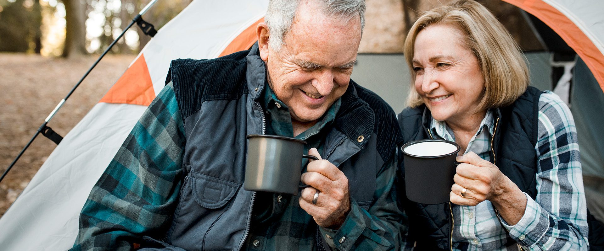 happy-elderly-couple-having-coffee-by-tent-forest