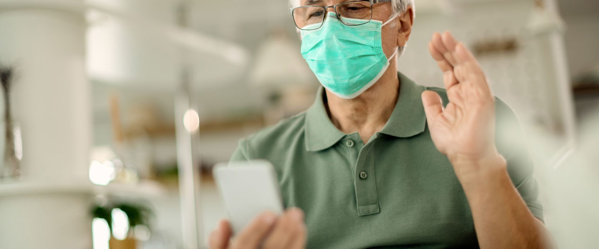 senior-man-with-face-mask-waving-while-making-video-call-smart-phone-home
